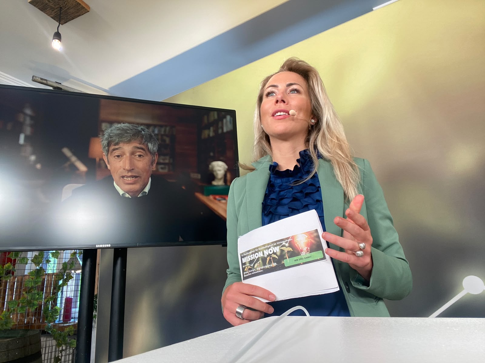 La Dra. Ines Marbach con micrófono de diadema durante una moderación online con un invitado conectado a distancia.
